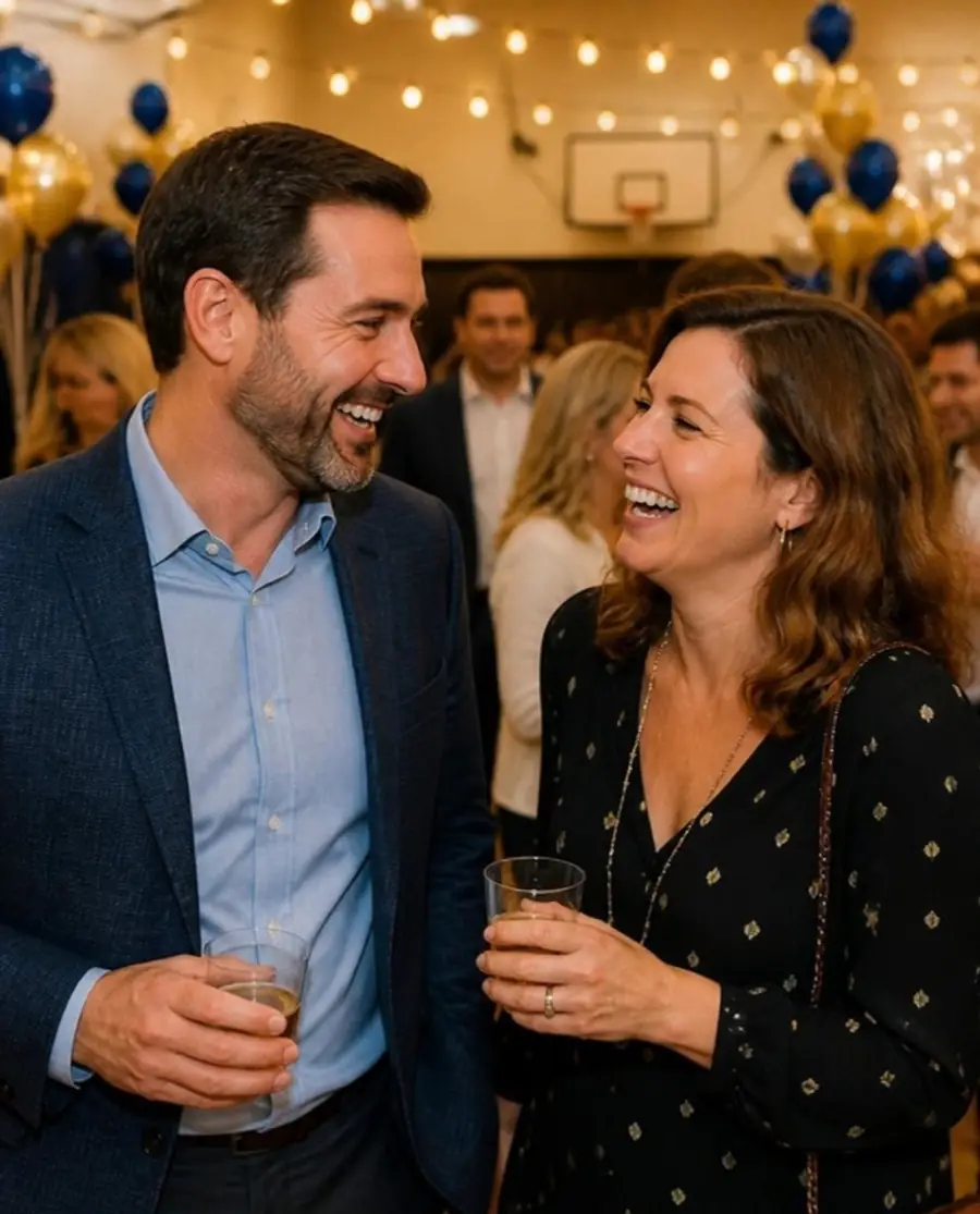 Two friends laughing over drinks at a class reunion
